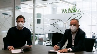 News Zwei Männer mit Schutzmasken sitzen an einem Tisch und unterzeichnen Dokumente in einem Büro