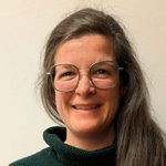 Unterpustertal/Gadertal Porträt einer lächelnden Frau mit langen braunen Haaren und Brille vor weißer Wand