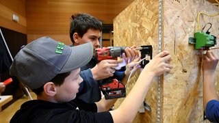 News Zwei Jugendliche montieren eine elektrische Installation auf einer Holzplatte