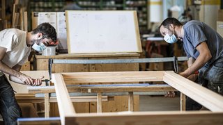 News Zwei Handwerker mit Masken montieren einen Holzrahmen in einer Werkstatt