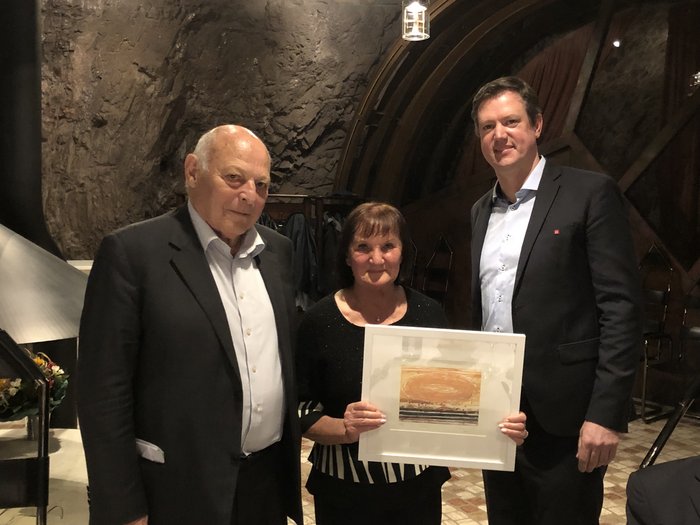 Ente Bilaterale: un doveroso riconoscimento ai protagonisti Tre persone in abiti eleganti in una stanza con parete rocciosa, donna con quadro incorniciato