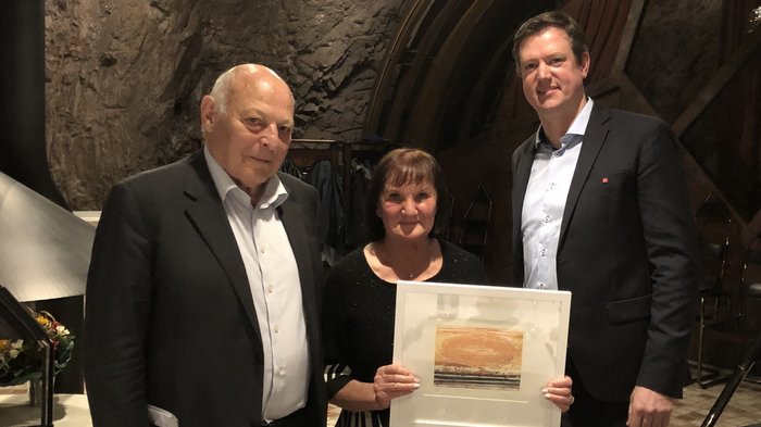 Bilaterale Körperschaft: verdiente Akteure geehrt Drei Personen in feiner Kleidung in einem Raum mit Felswand, Frau hält ein gerahmtes Bild