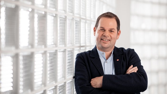 Presa di posizione sul sondaggio IPL: sostegno sociale sul posto di lavoro Uomo sorridente con le braccia incrociate davanti a parete di vetro