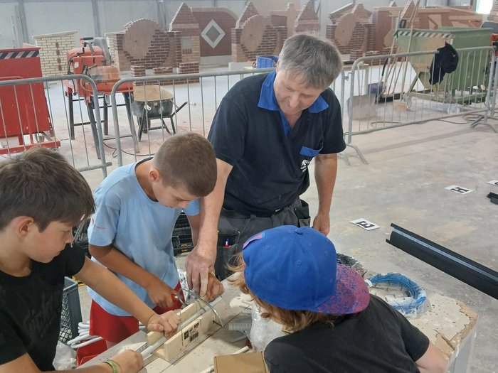 Mini-Baustelle, große Meisterwerke – KidsAcademy mauert in Bruneck Erwachsener zeigt Kindern handwerkliche Tätigkeit an Werkbank in Werkstatt