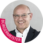 Klausen Porträt eines lächelnden Mannes mit Brille und Anzug vor grauem Hintergrund