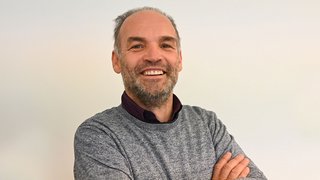 News Lächelnder Mann mit verschränkten Armen vor weißem Hintergrund