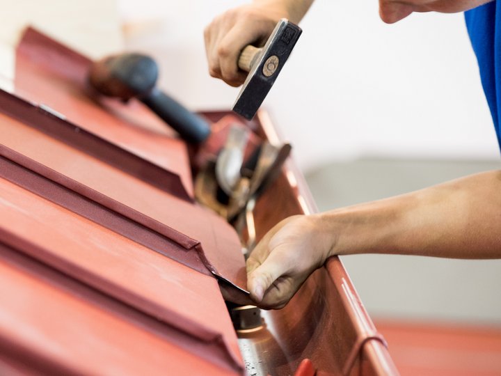 Lattonieri edili e artistici Operaio ripara tetto rosso con martello