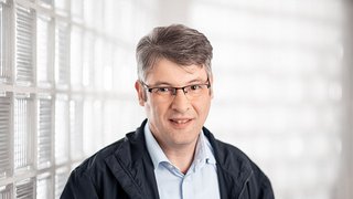 News Porträt eines Mannes mit Brille vor Glassteinwand