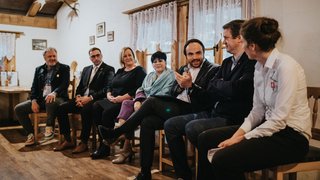 © Ivan Bortondello Sieben Personen diskutieren in einem gemütlichen Raum, einer hält ein Mikrofon