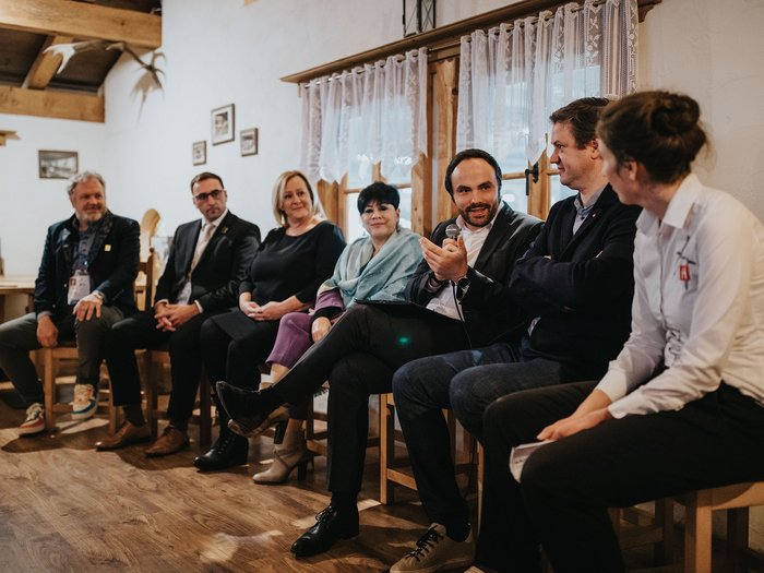 “Valorizziamo i punti di forza delle nostre aziende!” Sette persone discutono in una stanza accogliente, una tiene un microfono