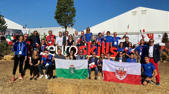 Junghandwerker on tour in Graz Gruppenfoto bei EuroSkills mit Menschen und Flaggen vor Zelt im Freien