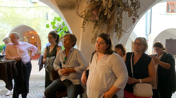 © Plattform Land Menschen stehen und hören unter einem Bogen mit Trockenblumen zu