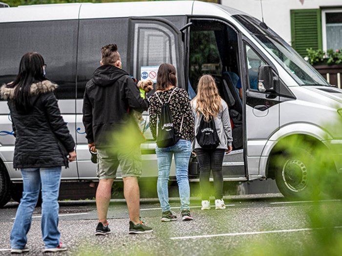 Thaler: „Schüler sind keine Pakete, die man einfach nicht abholt“ Menschen stehen in einer Schlange, um in einen Kleinbus einzusteigen