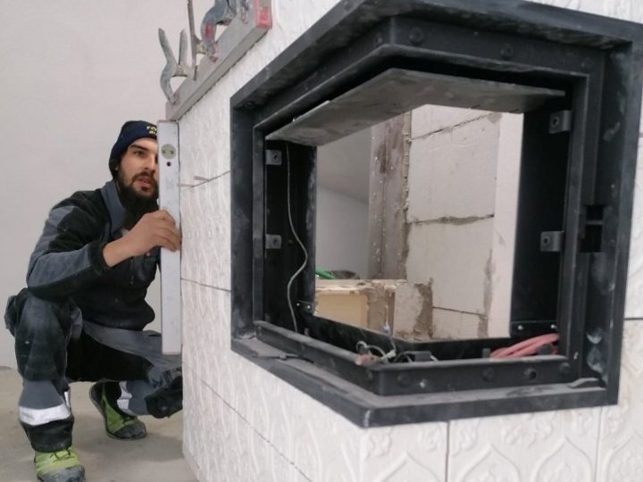 Fumisti Operaio installa un camino con piastrelle bianche e cornice metallica nera