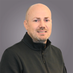 Das lvh-Team Porträt eines lächelnden Mannes mit Glatze und schwarzem Jacke vor grauem Hintergrund