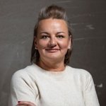 Bozen Land Porträt einer lächelnden Frau mit hellbraunem Pullover vor grauem Hintergrund