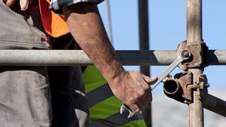 News Bauarbeiter zieht Schraube am Gerüst mit Schraubenschlüssel fest