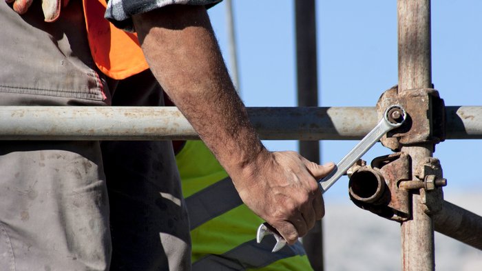Raum und Landschaft beschäftigt Ultner Handwerk Bauarbeiter zieht Schraube am Gerüst mit Schraubenschlüssel fest
