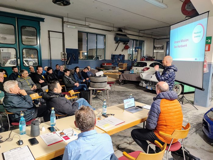 Aktiv und zukunftsorientiert: Das Handwerk in Auer Person hält Präsentation vor Publikum in einer Autowerkstatt
