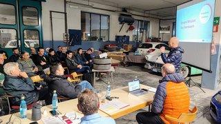News Person hält Präsentation vor Publikum in einer Autowerkstatt