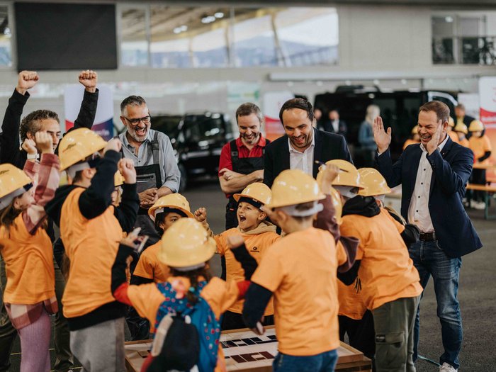 L‘iniziativa "Abenteuer Handwerk" (“Avventura Artigianato”) appassiona le giovani generazioni ai mestieri artigianali in Val Pusteria Bambini con caschi da lavoro festeggiano con adulti supervisori in uno spazio coperto