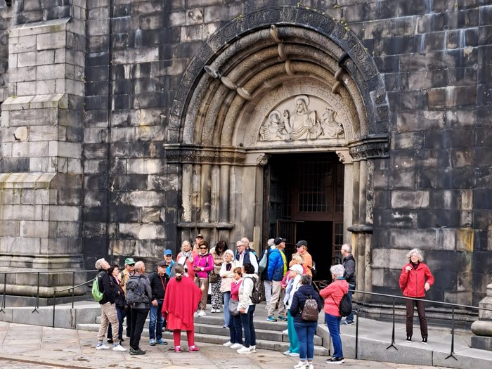 Reisefreudige Althandwerker/innen Gruppe von Touristen vor einem historischen Kirchentor mit Steinskulpturen