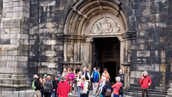 Reisefreudige Althandwerker/innen Gruppe von Touristen vor einem historischen Kirchentor mit Steinskulpturen