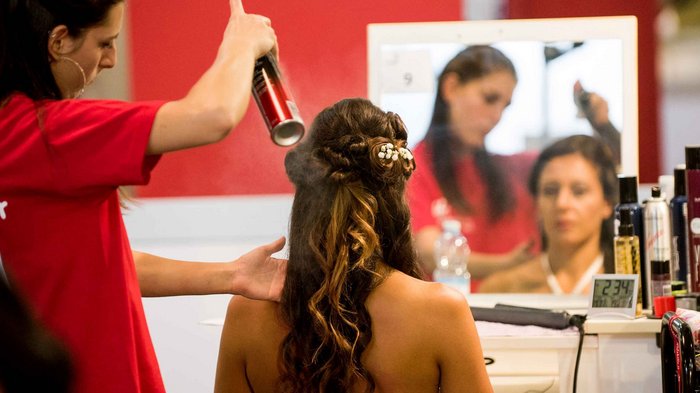 WorldSkills Italy: 115 junge Talente gehen am 1. Oktober an den Start Friseurin sprüht Haarspray auf geflochtene Hochsteckfrisur mit Blumen