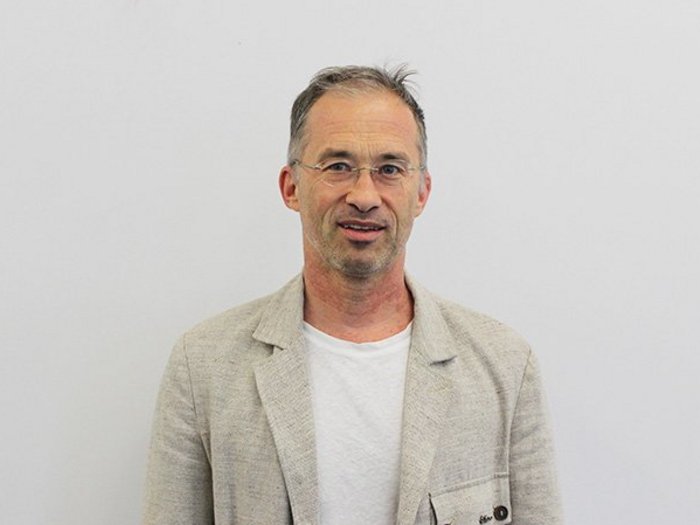 Meraner Handwerk sucht direkten Dialog Mann mit Brille trägt beige Sakko und weißes T-Shirt vor weißem Hintergrund