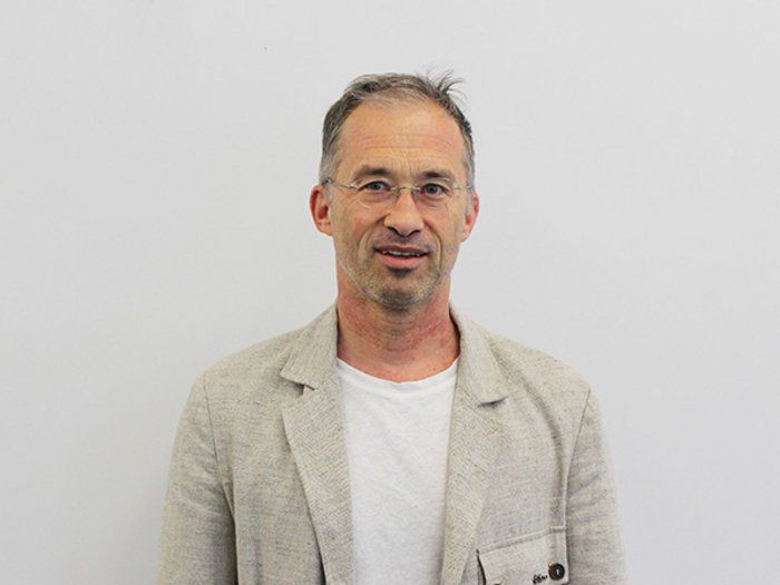 Meraner Handwerk sucht direkten Dialog Mann mit Brille trägt beige Sakko und weißes T-Shirt vor weißem Hintergrund