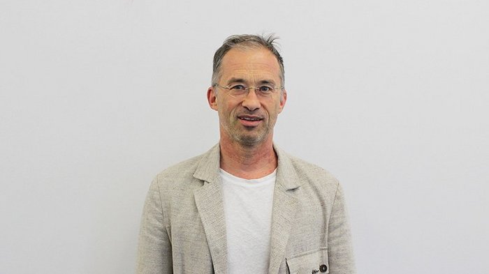 Meraner Handwerk sucht direkten Dialog Mann mit Brille trägt beige Sakko und weißes T-Shirt vor weißem Hintergrund