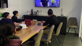 News Personen schauen eine Präsentation an einem Bildschirm in einem Besprechungsraum.