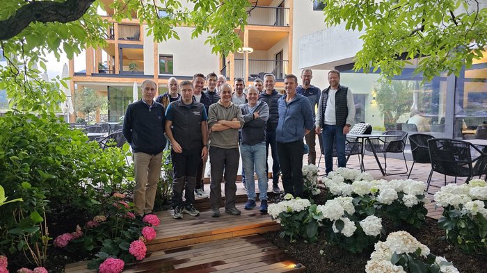 Scambio di competenze con gli insegnanti del Centro di formazione professionale di Brunico Gruppo di uomini in piedi su passerella di legno tra fiori e edifici