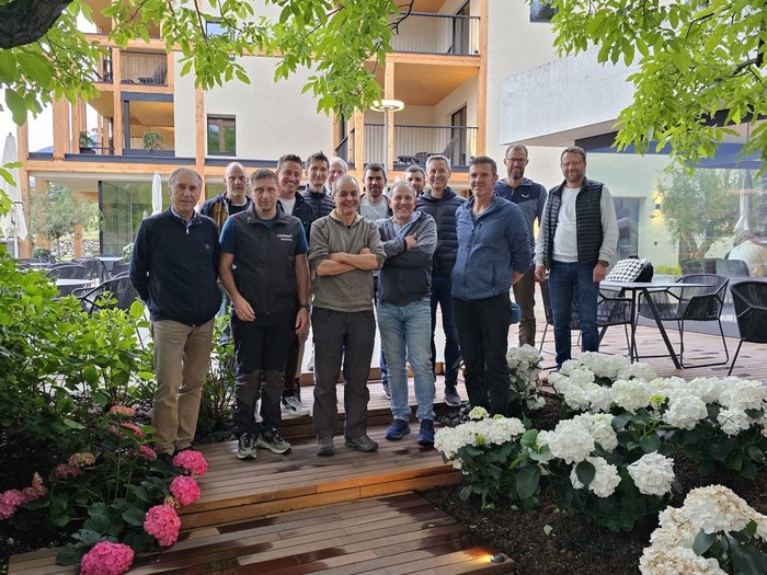 Fachaustausch mit Lehrpersonen des Berufsbildungszentrums Bruneck Gruppe von Männern steht draußen auf Holzsteg zwischen Blumen und Gebäuden