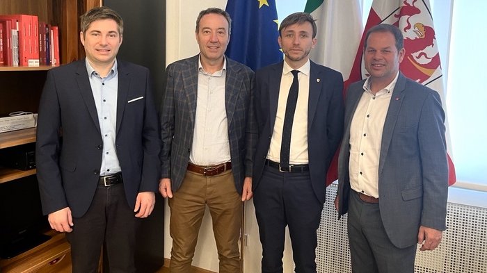 Stärkung des Handwerks durch partnerschaftliche Politik und neue Lösungsansätze Vier Männer in Anzügen stehen vor den Flaggen der EU, Italiens und Südtirols