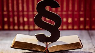 News Paragrafensymbol auf aufgeschlagenem Buch vor rotem Bücherregal