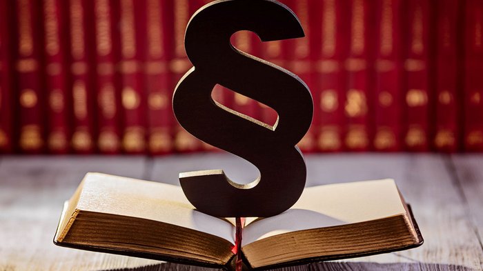 Il nuovo registro dei rifiuti Simbolo del paragrafo su libro aperto davanti a scaffale di libri rossi