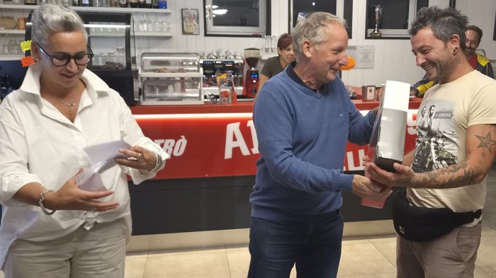 Edilizia 2027: cosa interessa ora a imprese e progettisti Un uomo anziano consegna un premio a un uomo in un bar, mentre una donna tiene dei fogli