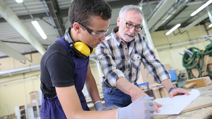 Handwerker als Impulsgeber und Mitgestalter vor Ort Älterer Mann erklärt jüngeren Mann Bauplan in Werkstatt