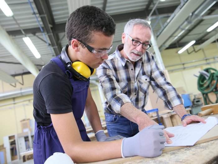 Handwerker als Impulsgeber und Mitgestalter vor Ort Älterer Mann erklärt jüngeren Mann Bauplan in Werkstatt