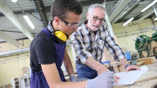 News Älterer Mann erklärt jüngeren Mann Bauplan in Werkstatt