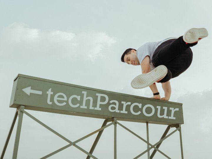 Soluzioni digitali Uomo che salta sopra il cartello TechParcour facendo parkour