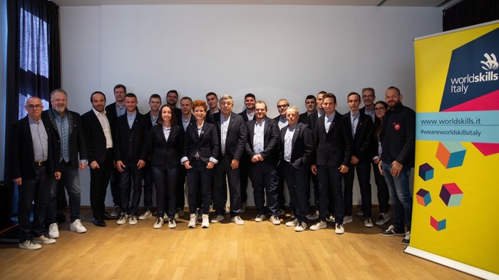 WorldSkills 2022: il Team Italy torna a gareggiare Foto di gruppo dei membri di WorldSkills Italy davanti allo striscione in abbigliamento formale casual