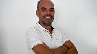 News Mann mit weißem Poloshirt lächelnd mit verschränkten Armen vor weißem Hintergrund