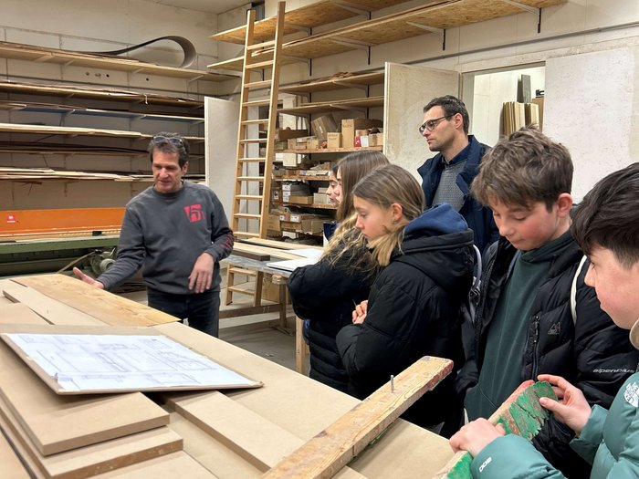 Handwerks- und Gastbetriebe im Fokus Gruppe in Holzwerkstatt hört Mann bei Erklärung mit Holzteilen und Zeichnungen zu