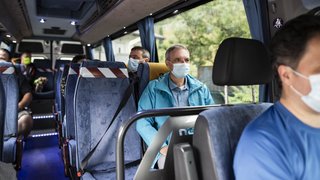 News Menschen mit Schutzmasken sitzen in einem Bus mit sozialen Distanzmaßnahmen