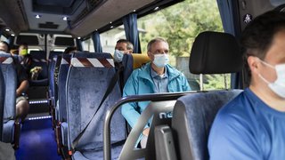 News Menschen mit Schutzmasken sitzen in einem Bus mit sozialen Distanzmaßnahmen