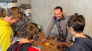 News Erwachsener erklärt Jugendlichen Werkzeuge auf Werkbank in Werkstatt