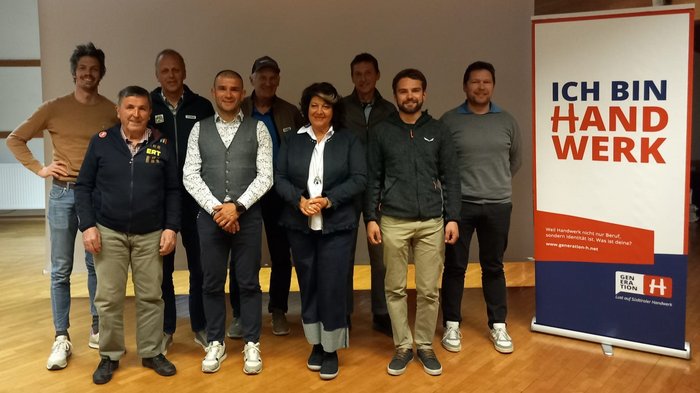 Junge Mütter und Unternehmerinnen starten Coworking mit Kinderbetreuung Gruppe von neun Erwachsenen vor einer Ich bin Handwerk Werbetafel