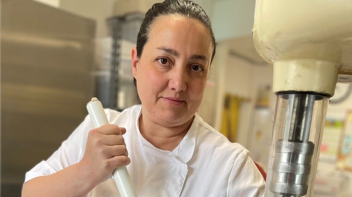 Mehr als nur eine Kugel Genuss: Warum handwerkliches Speiseeis die bessere Wahl ist Frau in weißer Kochjacke rührt mit großem Stab in Metallbehälter in Küche